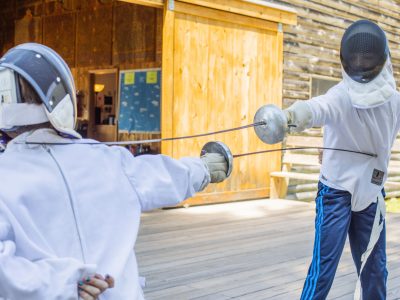 Two campers in protective gear competing in a fencing bout.