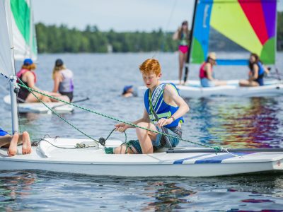A camper learning to sail a sailboat on a calm lake.