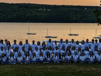 All staff photo in front of the sun setting on Thompson Lake.