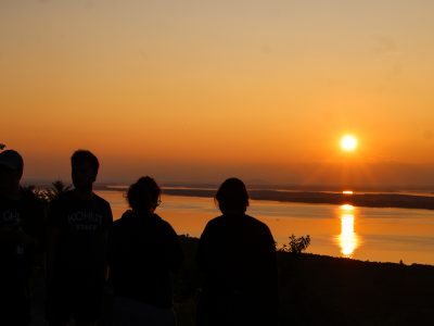 A silhouetted group of campers and counselors standing on a mountain peak watching a sunset of the Atlantic Ocean