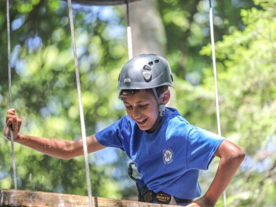 A camper wearing a helmet and harness navigating a challenging element of a high ropes course.